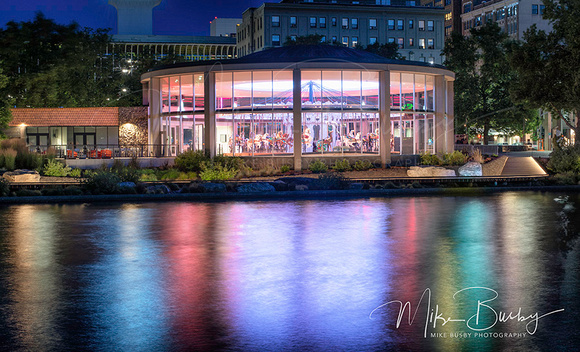 A photo of the Spokane Carousel at night with rainbow colors reflected on the water.