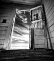 A black and white photograph of an old door looking out into desert farmland. 